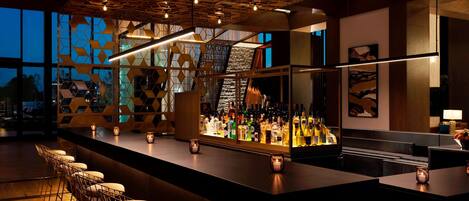 Zona de bar con una barra larga, varios taburetes y una amplia variedad de botellas.