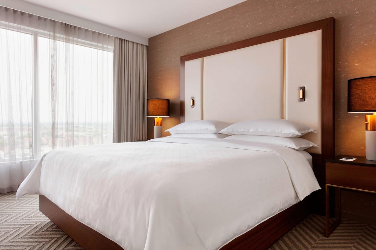 A hotel room with a large bed, two bedside lamps, a nightstand, and a view through the window.
