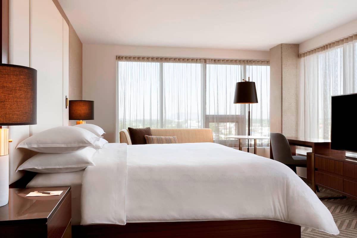 A hotel room with a large bed, a desk, a chair, a television, and a window with curtains.