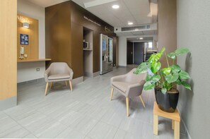 Un área de recepción con dos sillas, una planta en maceta, un tablón de anuncios y una máquina expendedora.