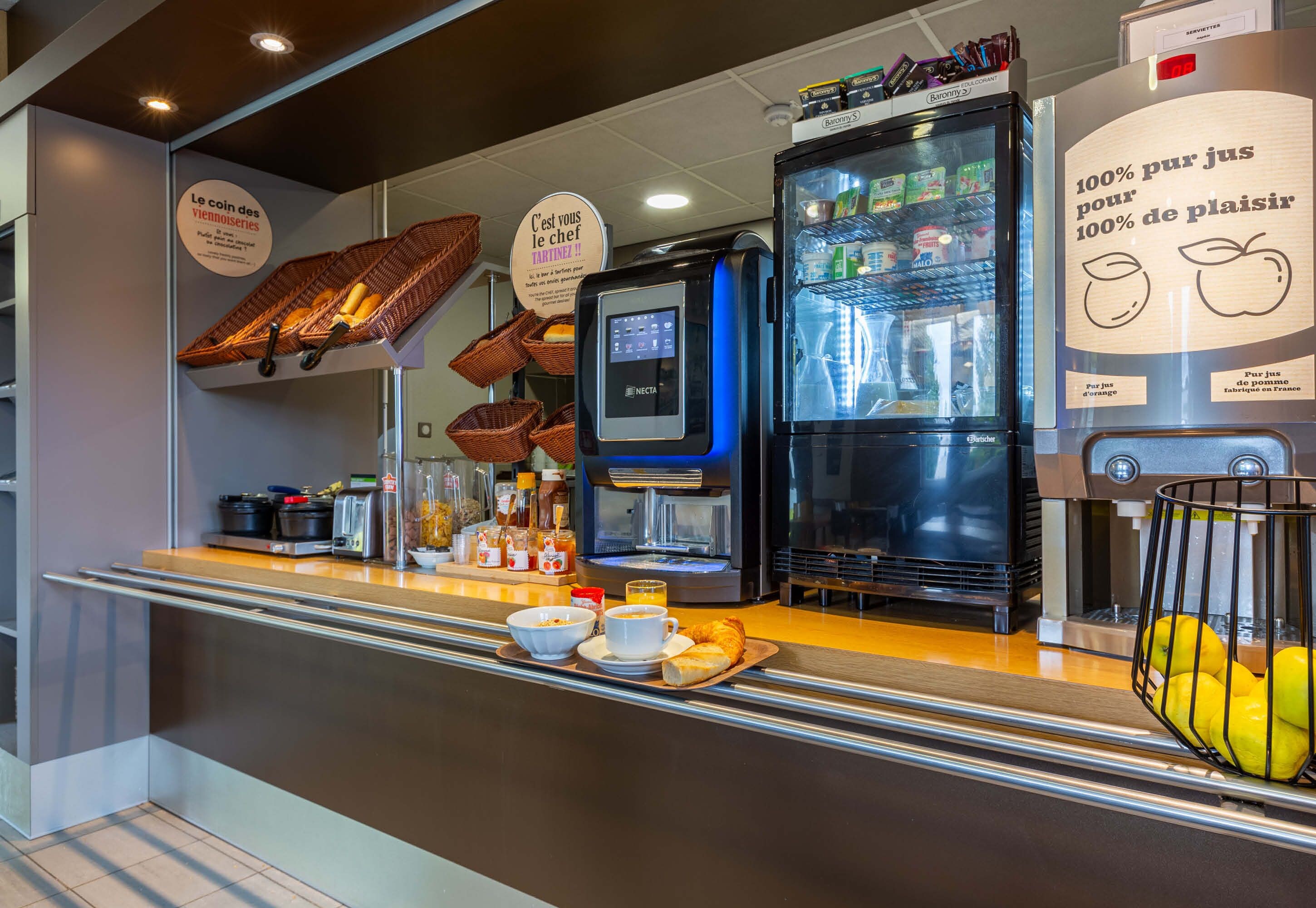A breakfast bar with a coffee machine, refrigerator, and baskets of bread.
