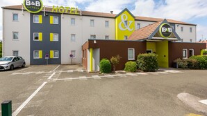 A B&B hotel with a yellow and brown facade, multiple windows, and a parking lot. - B&B Hotel Chartres 2 Le Coudray (Le Coudray)