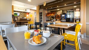 A breakfast area with tables, chairs, a coffee machine, and a display case with pastries. - B&B Hotel Chartres 2 Le Coudray (Le Coudray)