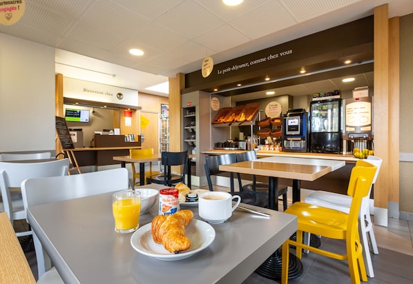A breakfast area with tables, chairs, a coffee machine, and a display case with pastries. - B&B Hotel Chartres 2 Le Coudray (Le Coudray)