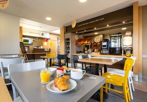 Un área de desayuno con mesas, sillas, una cafetera y un mostrador con pasteles.