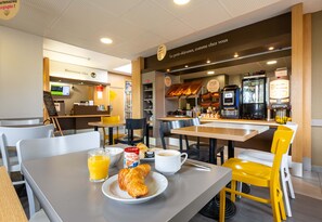 En frukostplats med bord, stolar, en kaffemaskin och ett vitrinskåp med bakverk.