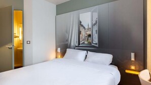 A hotel room with a bed, a painting of a street scene on the wall, and bedside lamps. - B&B Hotel Chartres 2 Le Coudray (Le Coudray)