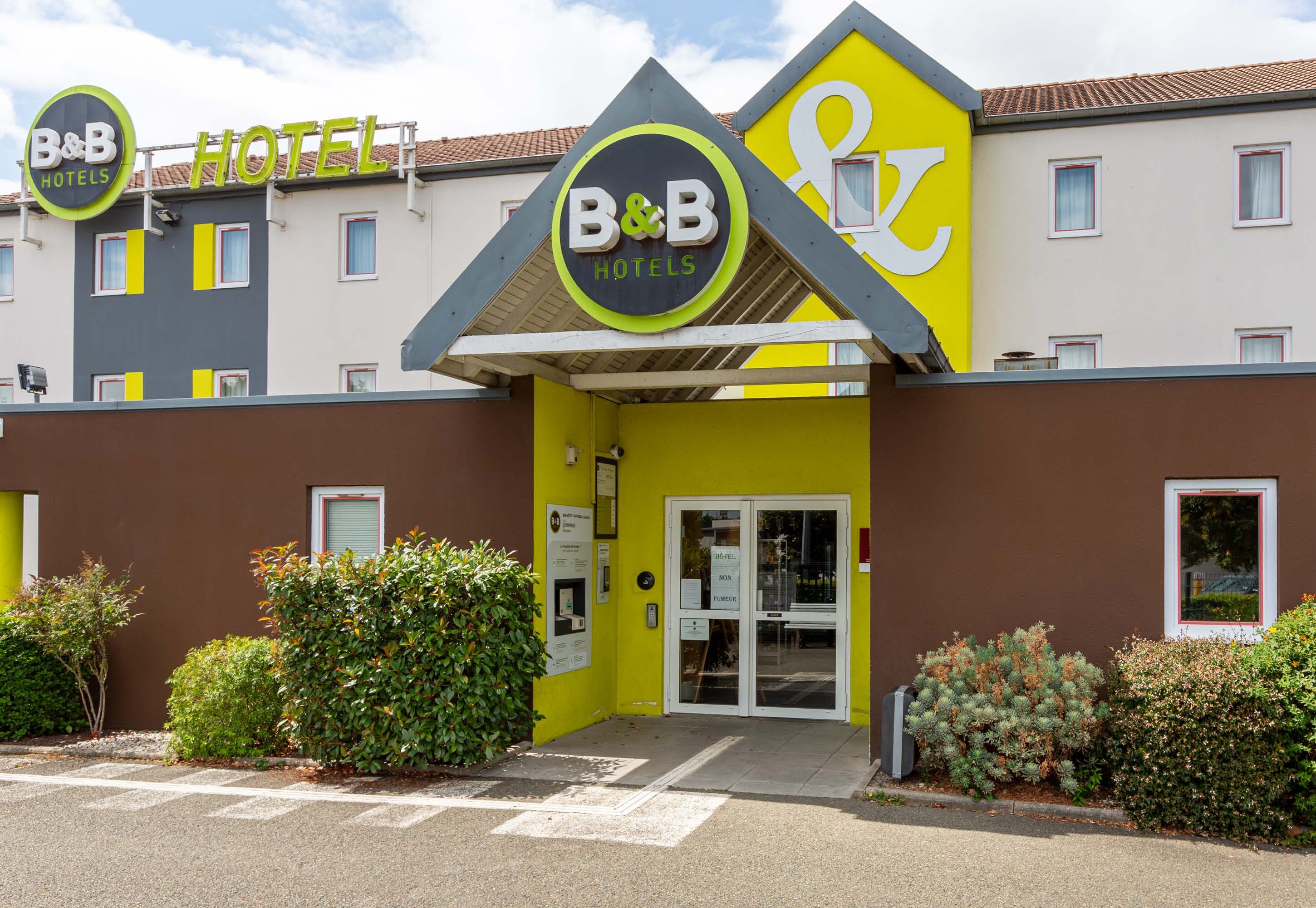 Un hotel tipo B&B con fachada amarilla, un letrero y una entrada con puerta de reja.