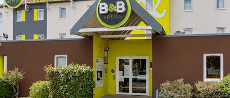Un hotel tipo B&B con fachada amarilla, un letrero y una entrada con puerta de reja.