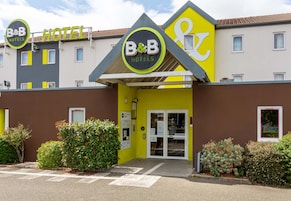 Un hotel tipo B&B con fachada amarilla, un letrero y una entrada con puerta de reja.