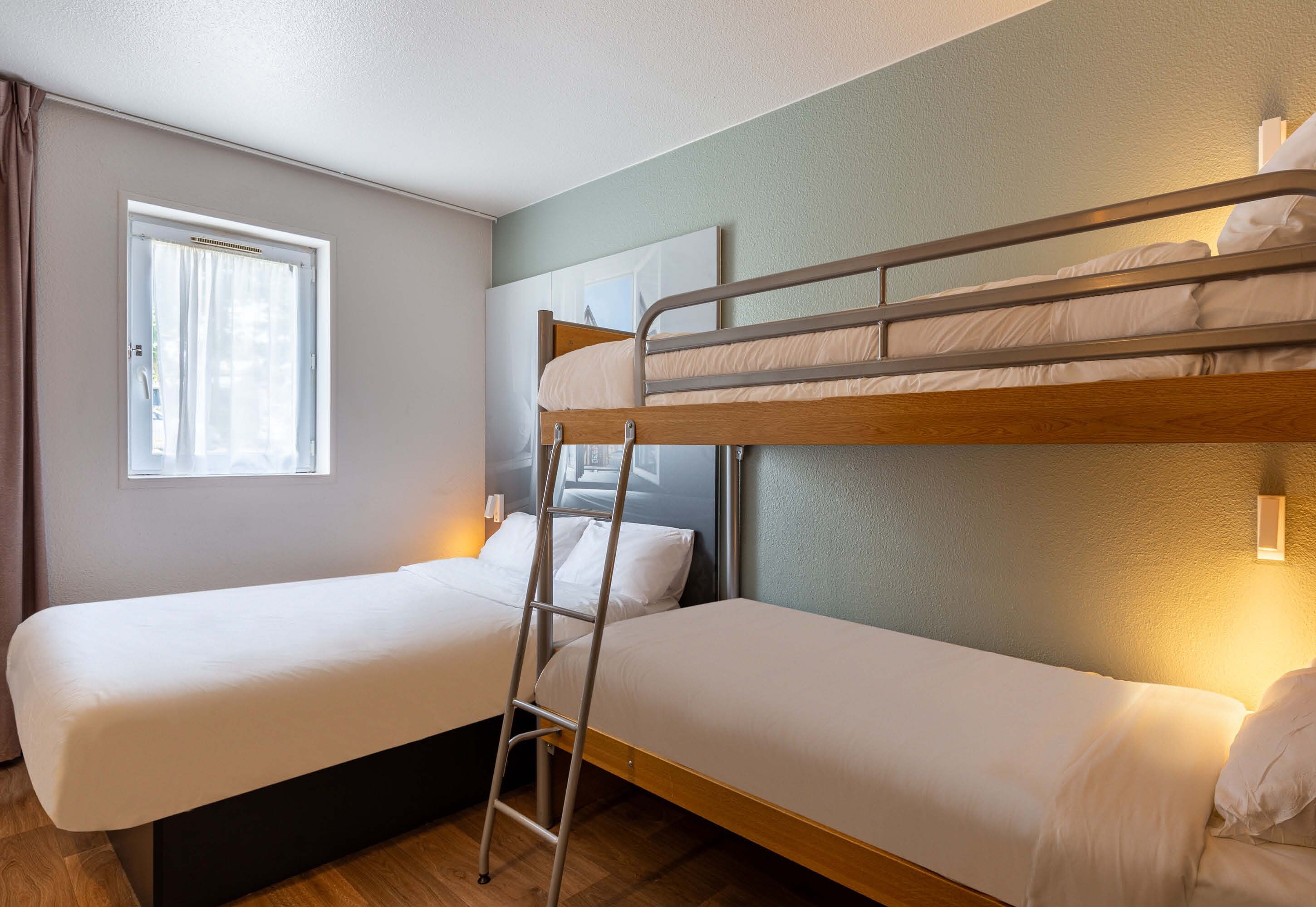 Una habitación con dos literas, una ventana con cortinas y una lámpara fijada a la pared.