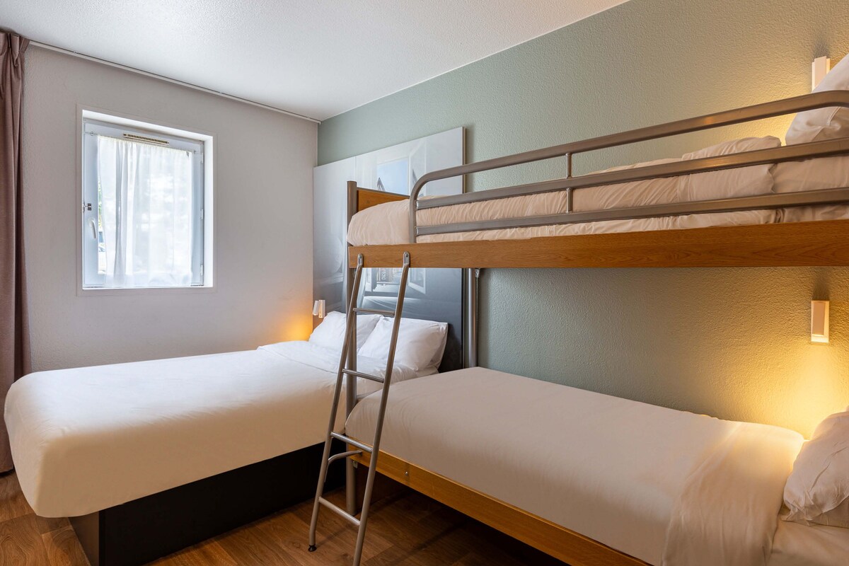 A room with two bunk beds, a window with curtains, and a wall-mounted light.