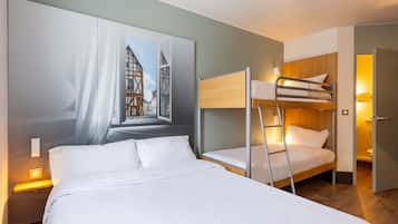 A hotel room with a bunk bed, a large window with a view of a building, and a bedside lamp.