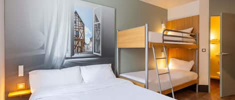 A hotel room with a bunk bed, a large window with a view of a building, and a bedside lamp.