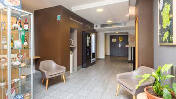 Eine Hotelhalle mit Sitzgelegenheiten, einer Glastheke, einem Kühlschrank und einer Zimmerpflanze.