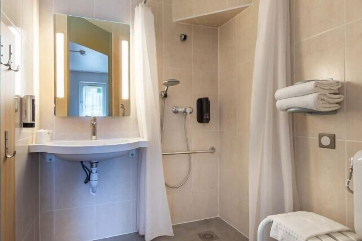 A bathroom with a sink, mirror, shower, and towel rack.