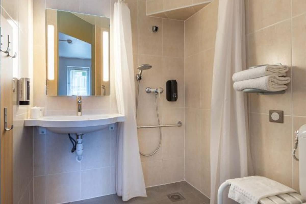 A bathroom with a sink, mirror, shower, and towel rack.