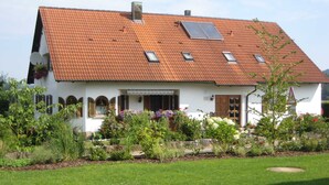 Ein weißes Haus mit rotem Ziegeldach, einem kleinen Garten und einem Rasen.