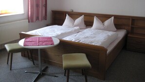 Ein Doppelbett mit weißer Bettwäsche, zwei Nachttische und ein runder Tisch mit pinkfarbener Tischdecke.