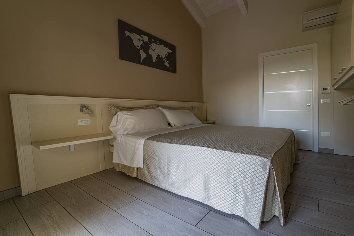 A bedroom with a bed, a world map on the wall, and a door with a light switch.