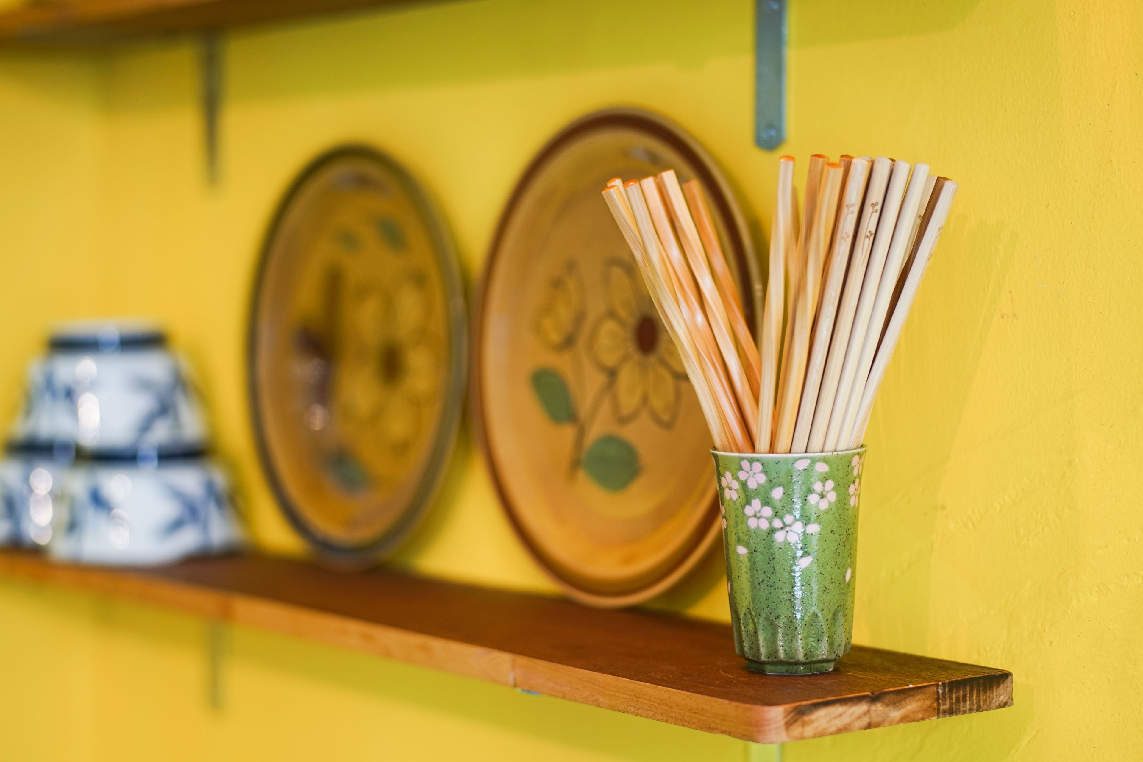 A shelf with a green cup holding wooden chopsticks, two decorative plates, and a blue and white container.