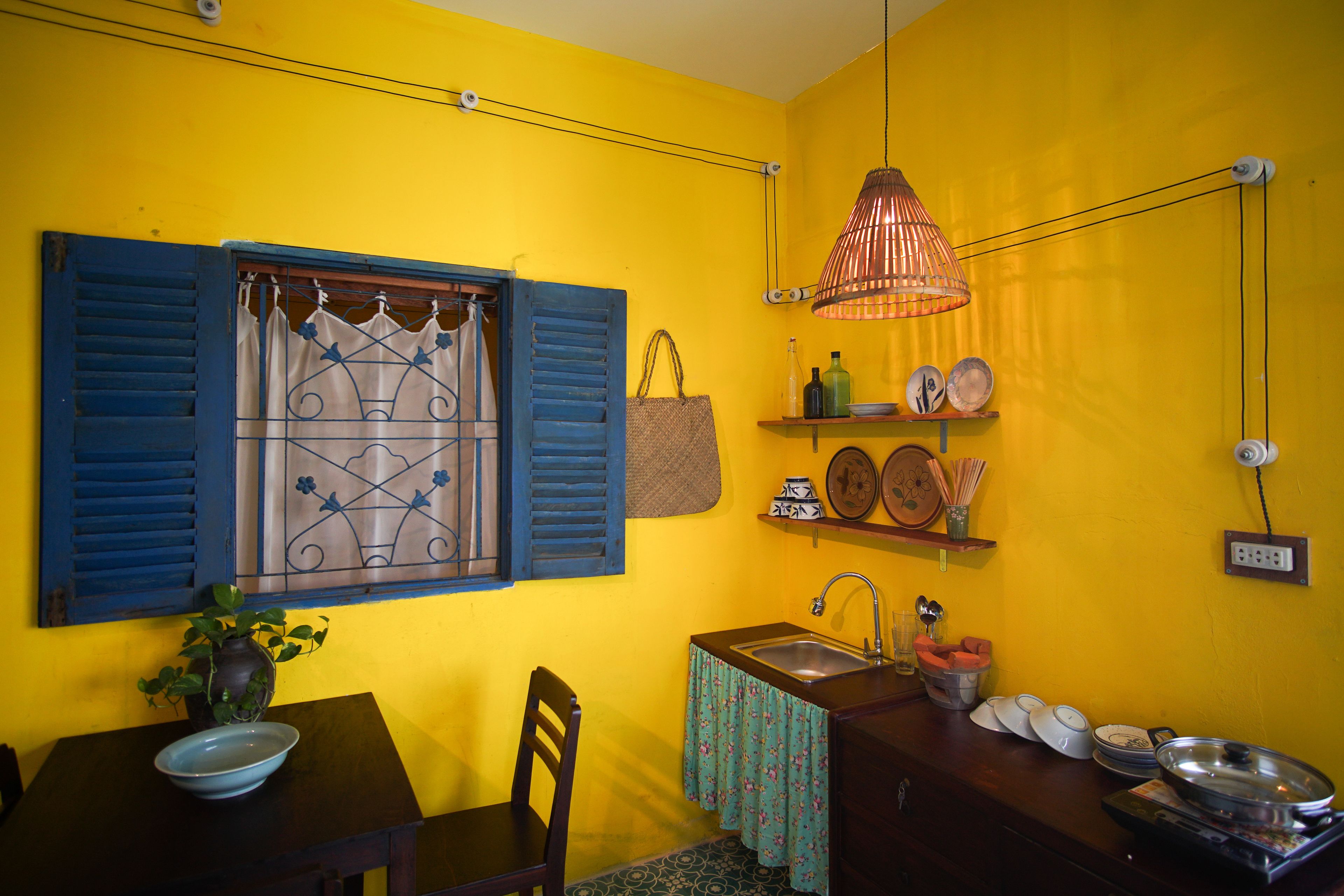 A compact kitchen with a sink, a dining table with a bowl, a chair, and a hanging light fixture.
