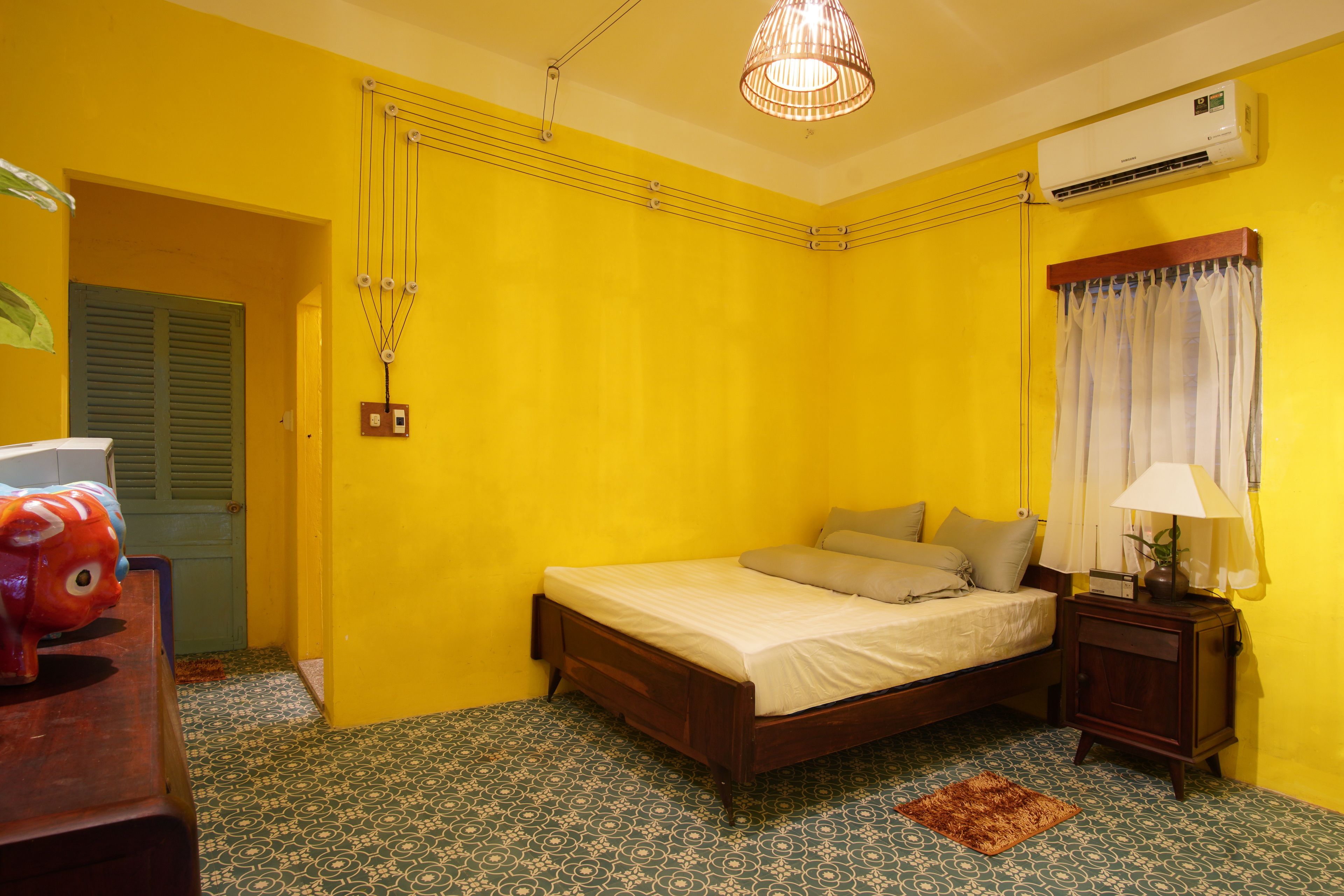 Una habitación con cama, mesita de noche, lámpara, lámpara colgante y aire acondicionado.