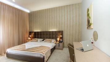 Een hotelkamer met een bed, nachtkastje, lamp, laptop en een bureau met een stoel.