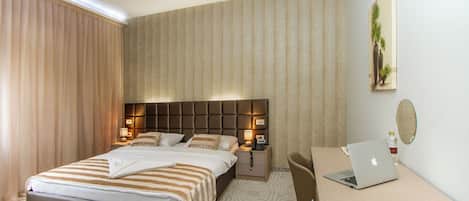 A hotel room with a bed, bedside table, lamp, laptop, and a desk with a chair.
