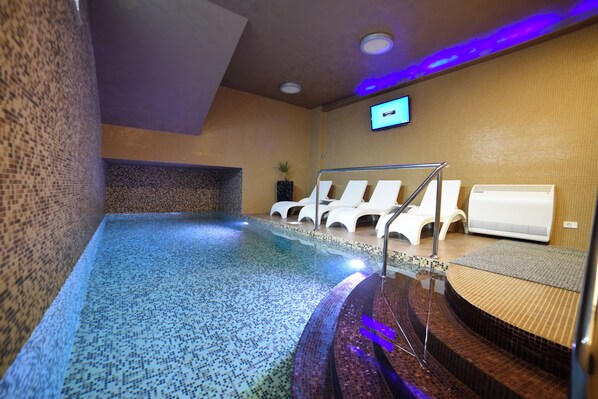 A spa area with a hot tub, lounge chairs, and a television screen.