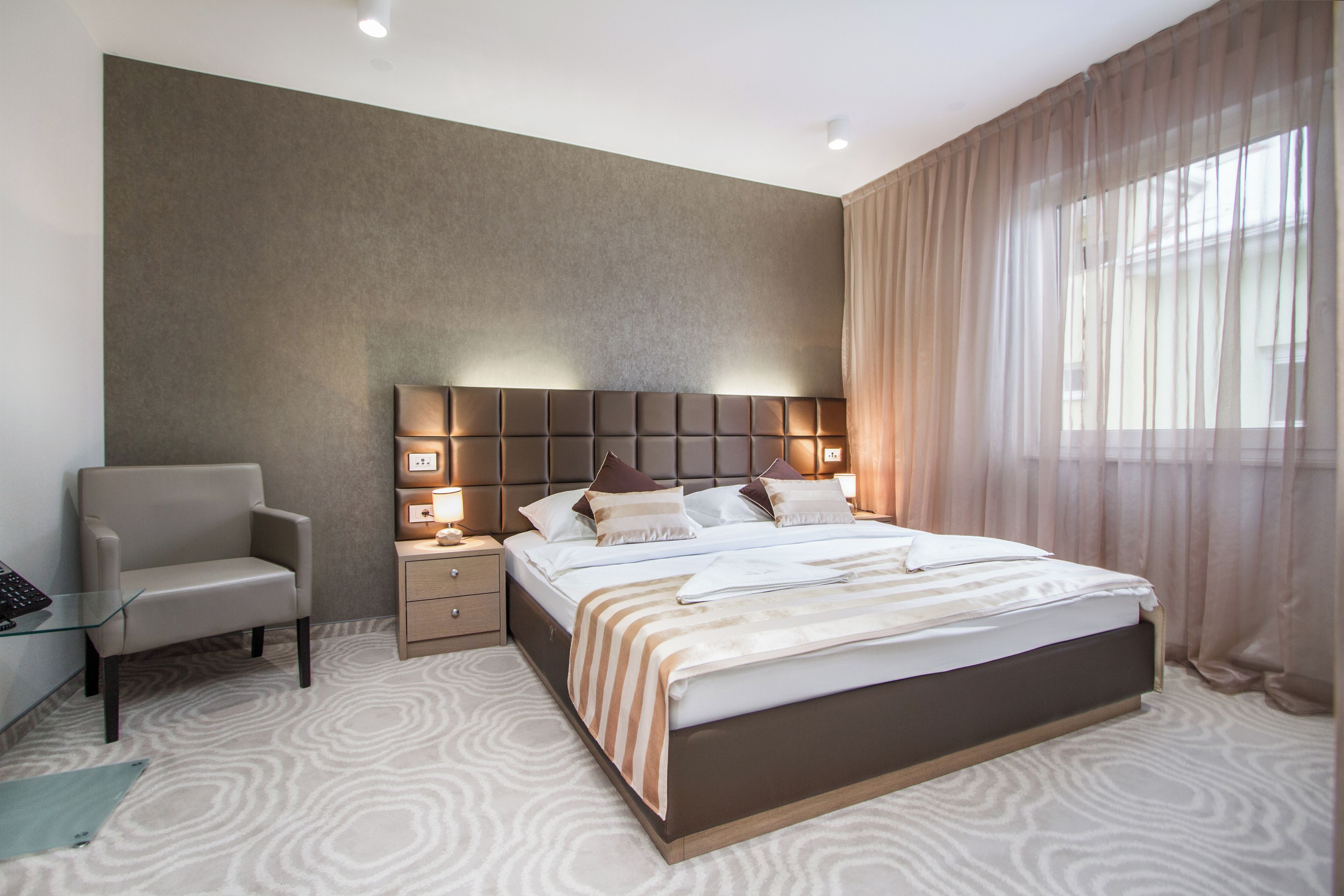 Una habitación de hotel moderna con una cama grande, una mesita de noche, una silla y un escritorio con una computadora.