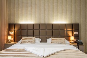 A neatly made bed with a striped bedspread, a headboard with illuminated panels, bedside lamps, and a telephone on the nightstand. - Royal Airport (Velika Gorica)