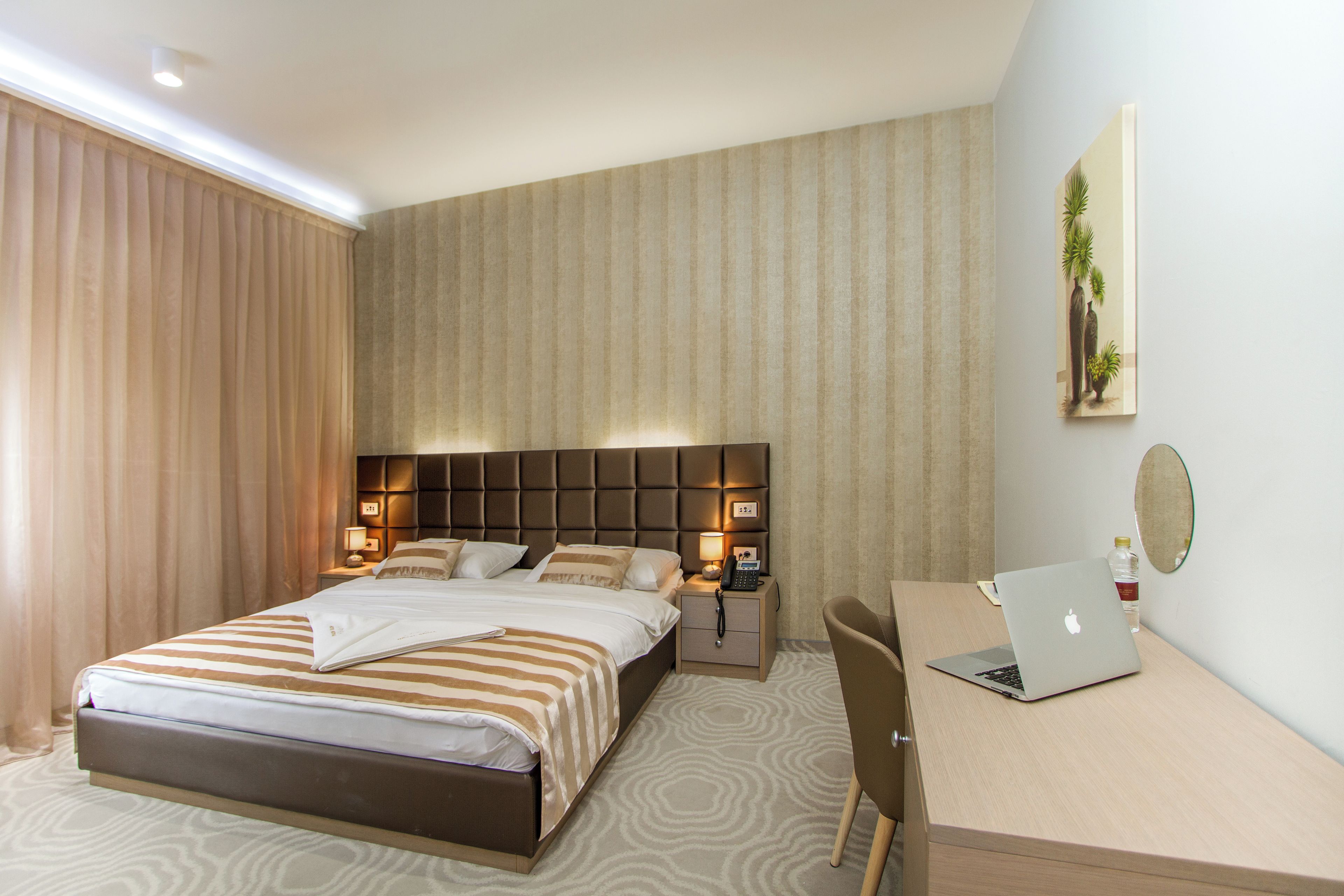 Una habitación de hotel con cama, mesita de noche, lámpara, computadora portátil y escritorio con silla.