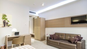 Habitació d'hotel moderna amb un llit, escriptori amb un ordinador portàtil, televisió penjada a la paret i un sofà amb coixins.