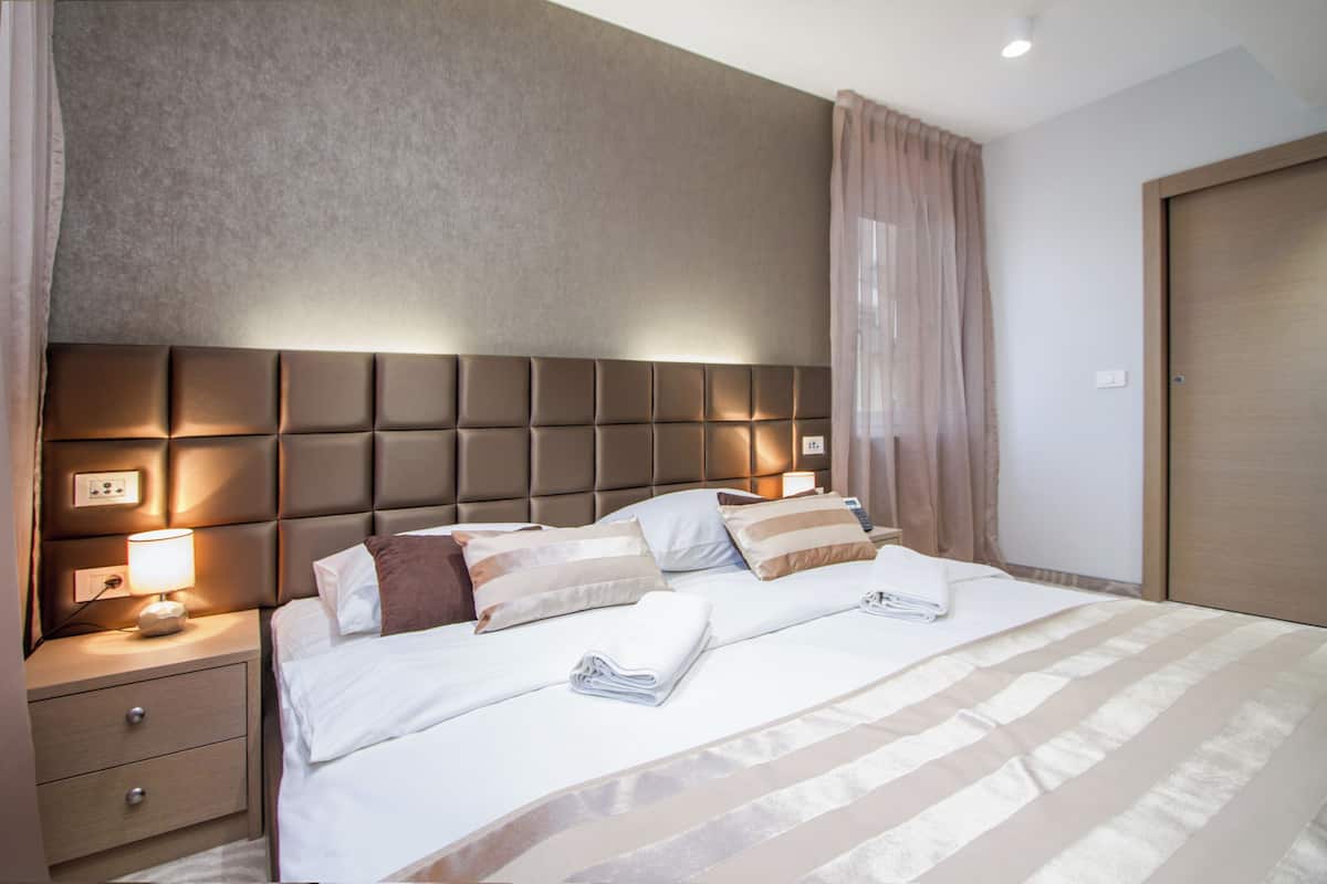 Une chambre d’hôtel avec un grand lit, une table de chevet avec une lampe, une prise de courant murale et une porte.
