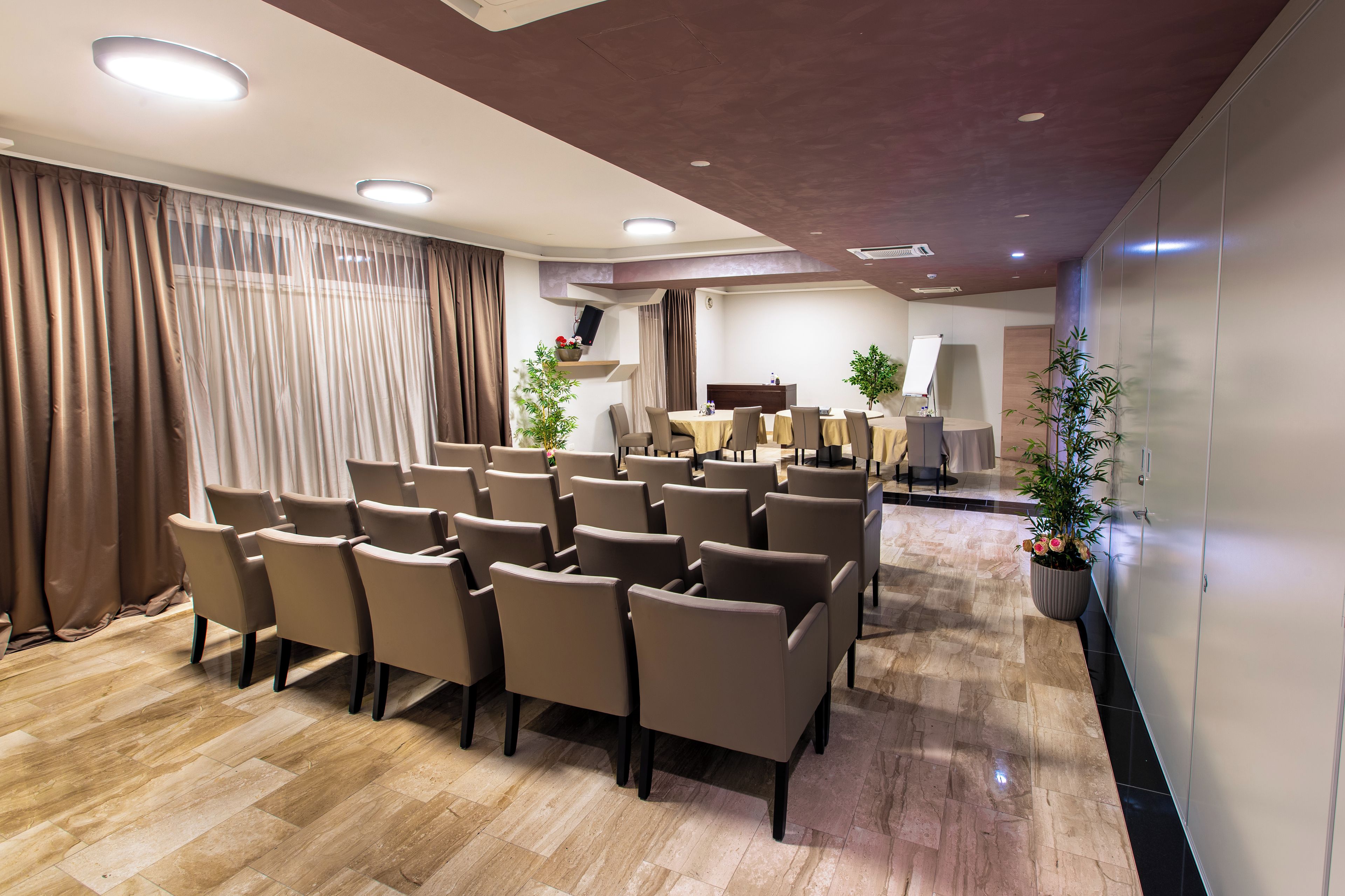 Un salón de conferencias con filas de sillas, un piano y plantas en macetas.