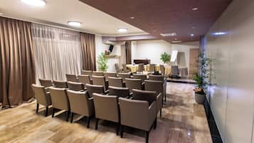 Un salón de conferencias con filas de sillas, un piano y plantas en macetas.