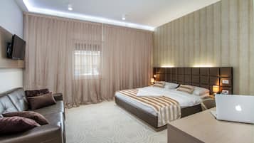 A modern hotel room with a bed, a desk with a laptop, a leather sofa, and a television.
