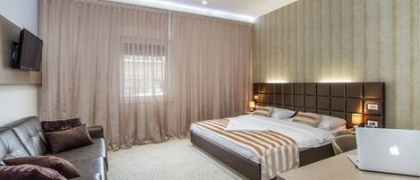 A modern hotel room with a bed, a desk with a laptop, a leather sofa, and a television.