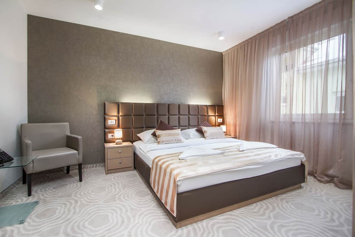 Une chambre d’hôtel moderne équipée d’un grand lit, d’une table de chevet, d’une chaise et d’un bureau avec un ordinateur.