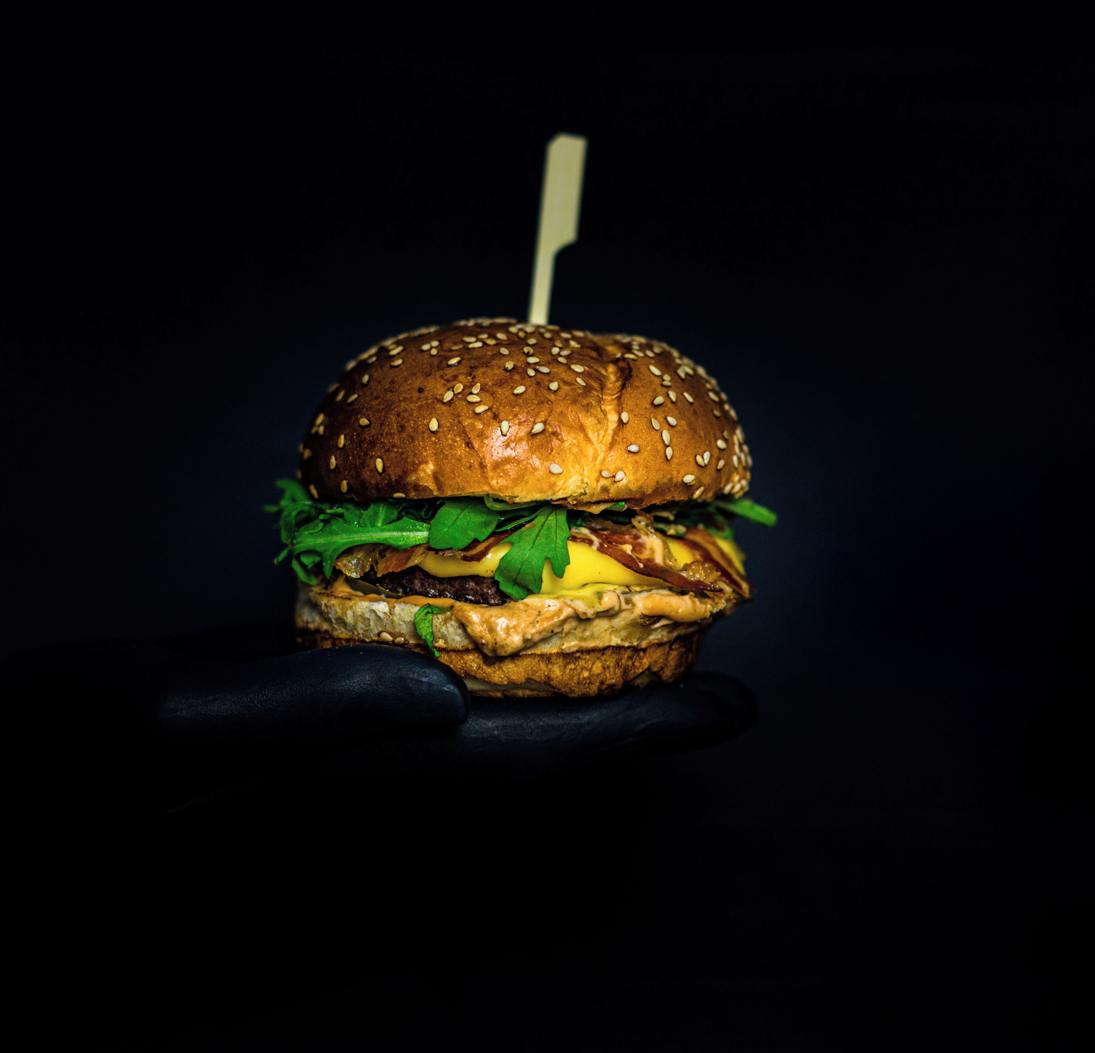 Una hamburguesa con pan de sésamo, lechuga, queso y un palillo.