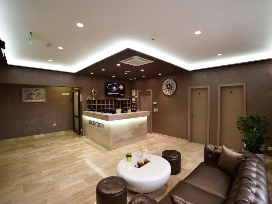 A hotel reception area with a reception desk, a clock, a sofa, and a potted plant.