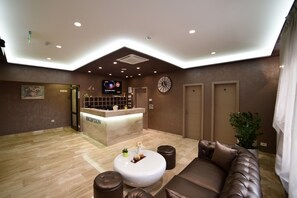 A hotel reception area with a reception desk, a clock, a sofa, and a potted plant.