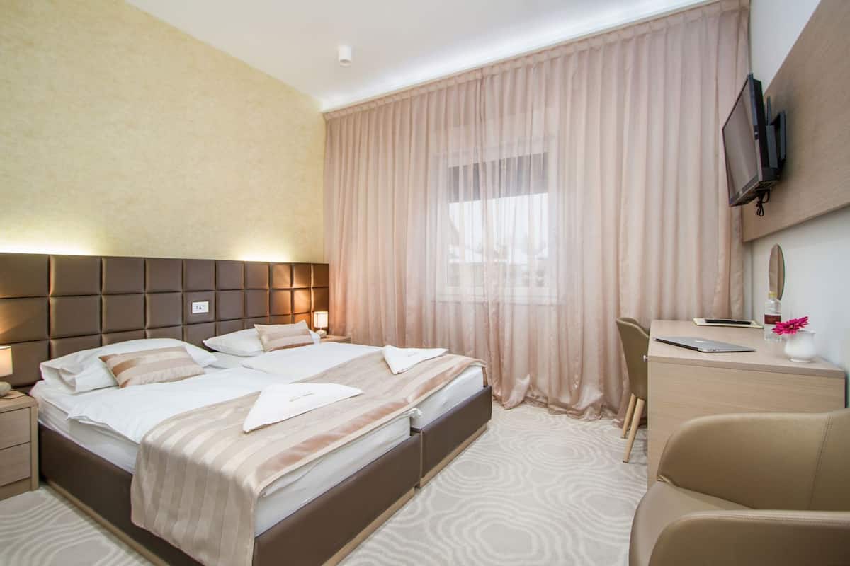 Une chambre d’hôtel avec un grand lit, un bureau, une chaise, une télévision et une fenêtre avec des rideaux.