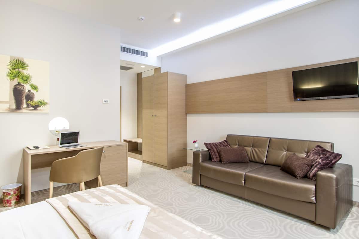 Une chambre d’hôtel moderne équipée d’un lit, d’un bureau avec un ordinateur portable, d’un téléviseur fixé au mur et d’un canapé.