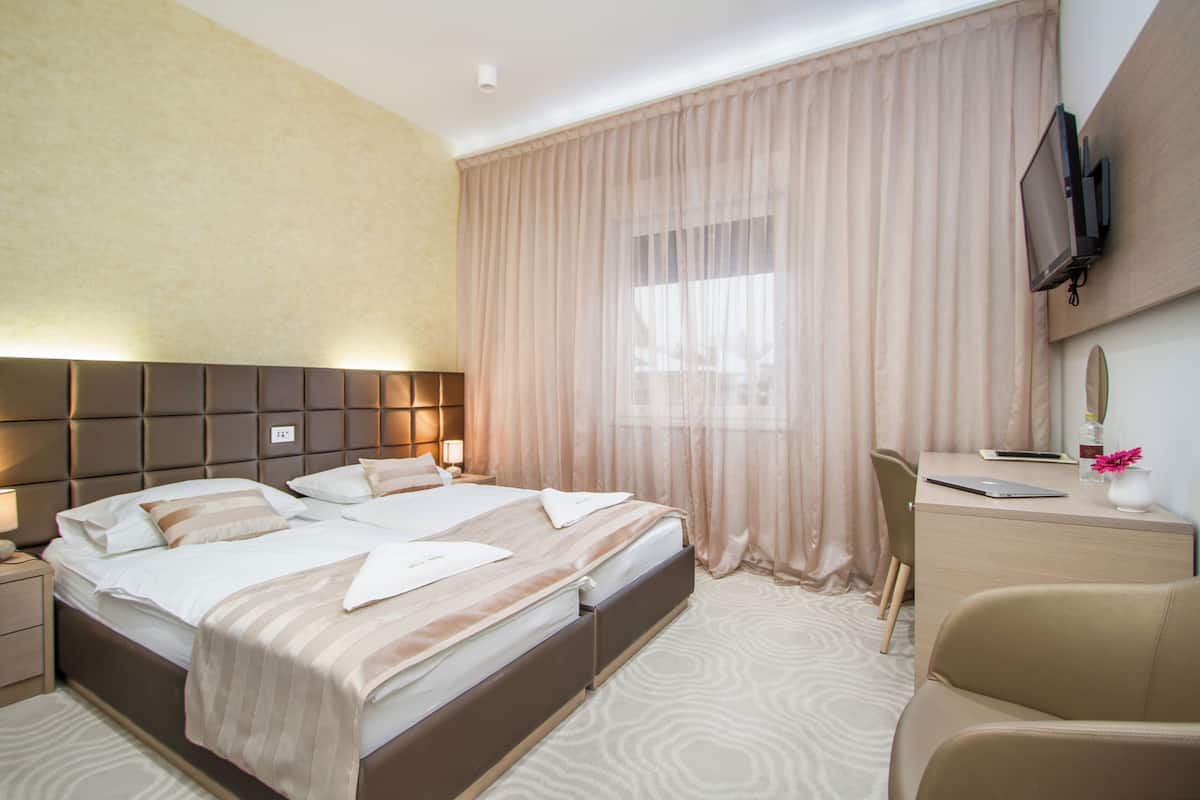 Une chambre d’hôtel avec un grand lit, un bureau, une chaise, une télévision et une fenêtre avec des rideaux.