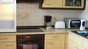 Et kompakt køkken med lyse træskabe, indbygget ovn, mikroovn og kaffemaskine.