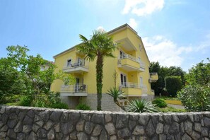 A yellow multi-story building with balconies, surrounded by greenery and a stone wall. - Studio with air conditioning (Malinska)