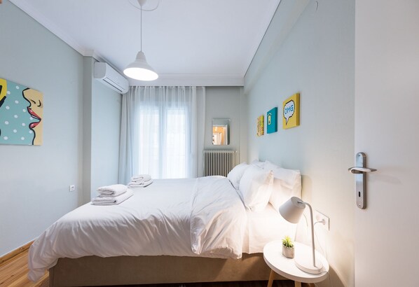A neatly made bed with white linens, a bedside lamp, and a small potted plant on a bedside table.