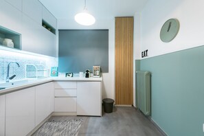 A modern kitchen with white cabinets, a sink, a coffee machine, and a clock on the wall.